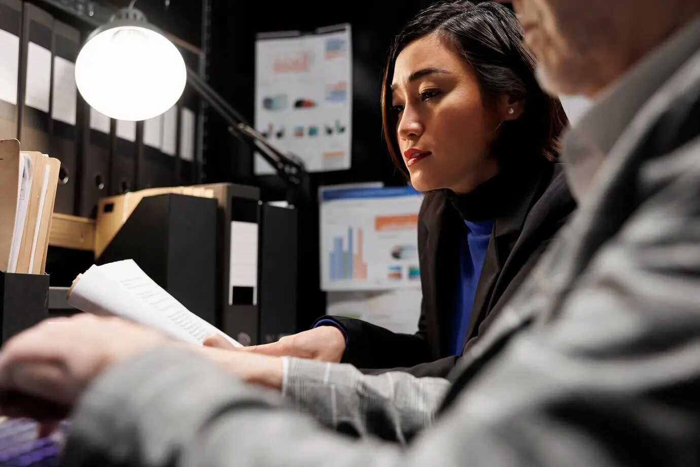 Коллеги-руководители в сфере бухгалтерского учета вводят в ноутбук аналитические данные по бухгалтерии. Пожилой бизнесмен и азиатский коллега работают в команде в административном архивном офисе-хранилище.